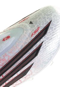 Focicipő fehér talppal, finom rózsamintákkal, fekete és piros háromcsíkos logóval, valamint piros "F50" felirattal a felső részen.