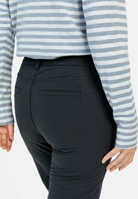 Sorte, tætsiddende bukser med en glat tekstur og elastisk talje, med to baglommer; båret med en lyseblå og hvid stribet top.