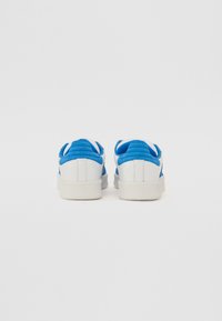 Hvite sneakers med blå detaljer, med en glatt skinnoverdel, polstret krage og teksturert gummisåle. Bakfra.