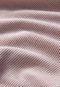Tissu côtelé rose clair avec de fines rayures horizontales, texture douce et surface lisse, présentant des ondulations et des plis délicats.