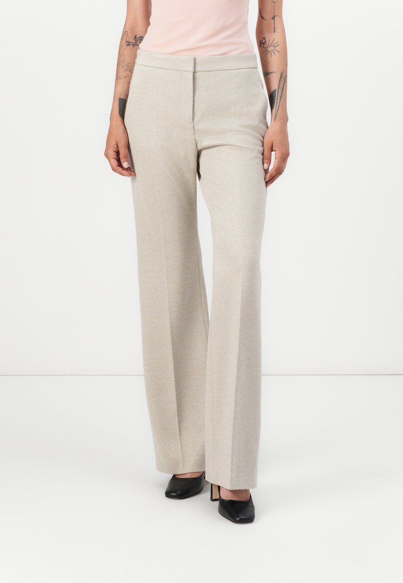 Hellbeige weite Hosen aus strukturiertem Stoff, mit hoher Taille und geradem Schnitt, kombiniert mit schwarzen High Heels.