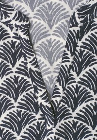 Gros plan d'un tissu avec un motif abstrait de feuille noir et blanc et un col en V.