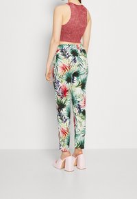 Femme portant un crop top rouge sans manches, un pantalon à imprimé tropical multicolore et des sandales à plateforme roses à talons hauts, se tenant dos.