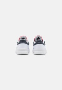 Sneakers bianchi con una superficie liscia, con accenti blu navy e rossi sul tallone. Logo impresso sul lato. Forma arrotondata.