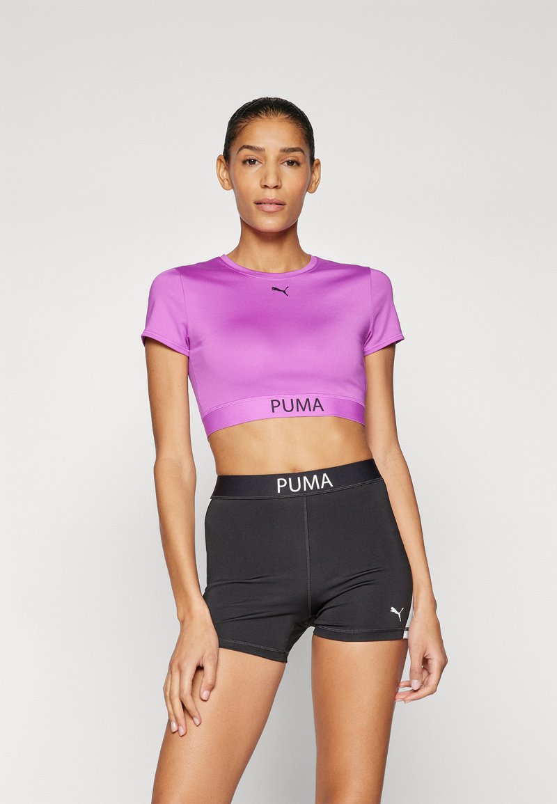 Violet trumpas sportinis marškinėlis su trumpomis rankovėmis, puošiamas juodu logotipu. Suderintas su juodomis aukšto juosmens šortais, ant kurių baltomis raidėmis išspausdintas prekės ženklas.