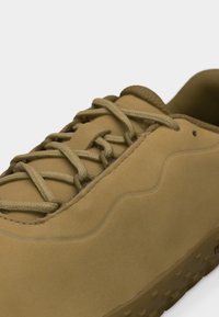 Ανοιχτό καφέ δερμάτινο αθλητικό παπούτσι με χοντρές στρογγυλές κορδόνια, επενδυμένο γιακά και υφασμένο πέλμα, σε κοντινή λήψη λεπτομέρειας.