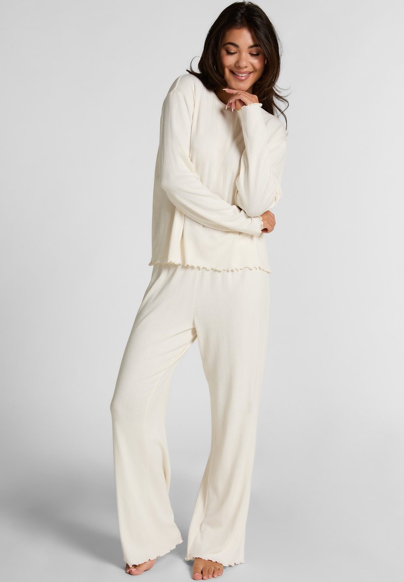 Crème-kleurige pyjama set van lichtgewicht, textuurstof. Heeft lange mouwen, een ontspannen pasvorm top en wijde broekspijpen met rafelige randen.