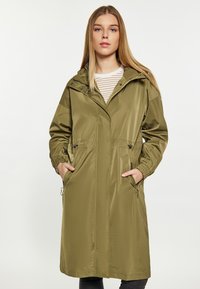 Olivgrön lång regnkappa med huva, elastiska ärmslut och två frontfickor. Tillverkad av ett slätt, vattenavvisande material.