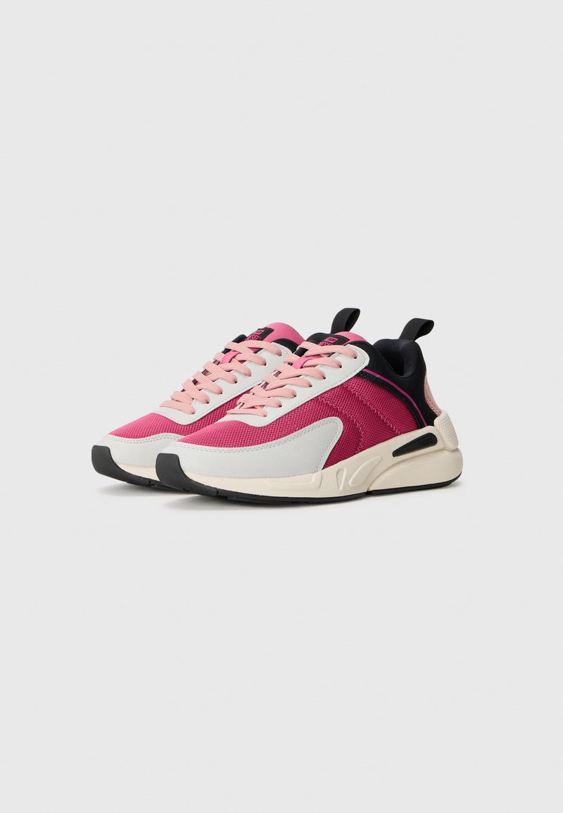 Des chaussures de sport avec un dessus en mesh rose et gris, des lacets roses, des accents de talon noirs et une semelle de couleur crème avec une semelle extérieure noire texturée.
