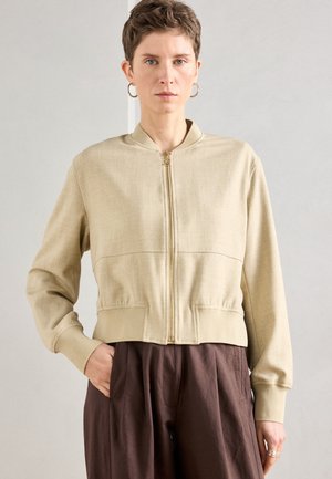 Beezh salatilmajope, millel on ees tõmblukk, soonilised varrukapaarid ja ääred. Sile tekstuur, lühendatud lõige ja minimalistlik disain.