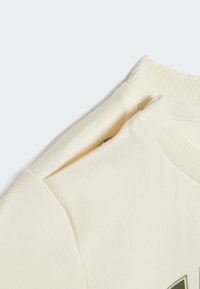Crèmekleurig katoenen T-shirt met een ribbelige ronde hals en korte mouwen, voorzien van een subtiele logo-accent in een contrasterende kleur. Gladde textuur.