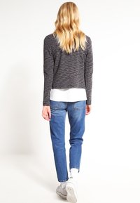 Haut à manches longues texturé gris de style court, associé à un jean en denim bleu. Le modèle porte des chaussettes blanches et des baskets gris clair.