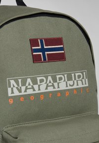 Zelený plátěný batoh s nášivkou norské vlajky v bordové a modré barvě. Logo "NAPAPIJRI geographical" v bílé a oranžové barvě.
