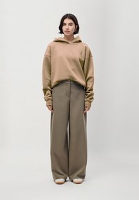 Felpa beige oversize con tasca a marsupio, abbinata a pantaloni larghi color verde oliva e sneakers chiare.