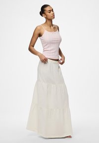 Světle růžový žebrovaný top na ramínka s nastavitelnými popruhy, spárovaný s krémovou maxi sukní ve vrstvách, která má elastický pas a jemnou texturu.