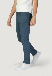 Pantalones azul marino de hombre, ajustados y elásticos, con cinco bolsillos y detalles de costura sutiles. Combinados con zapatillas blancas.