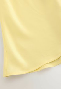 Tissu satin jaune avec une texture lisse et un ourlet incurvé. Les coutures sont visibles le long des bords, créant une finition nette.