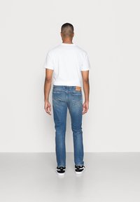 Blå denimjeans med slim fit, med lätt blekning, bakfickor och en brun läderlogga. Kombinerad med en vit t-shirt och svarta sneakers.