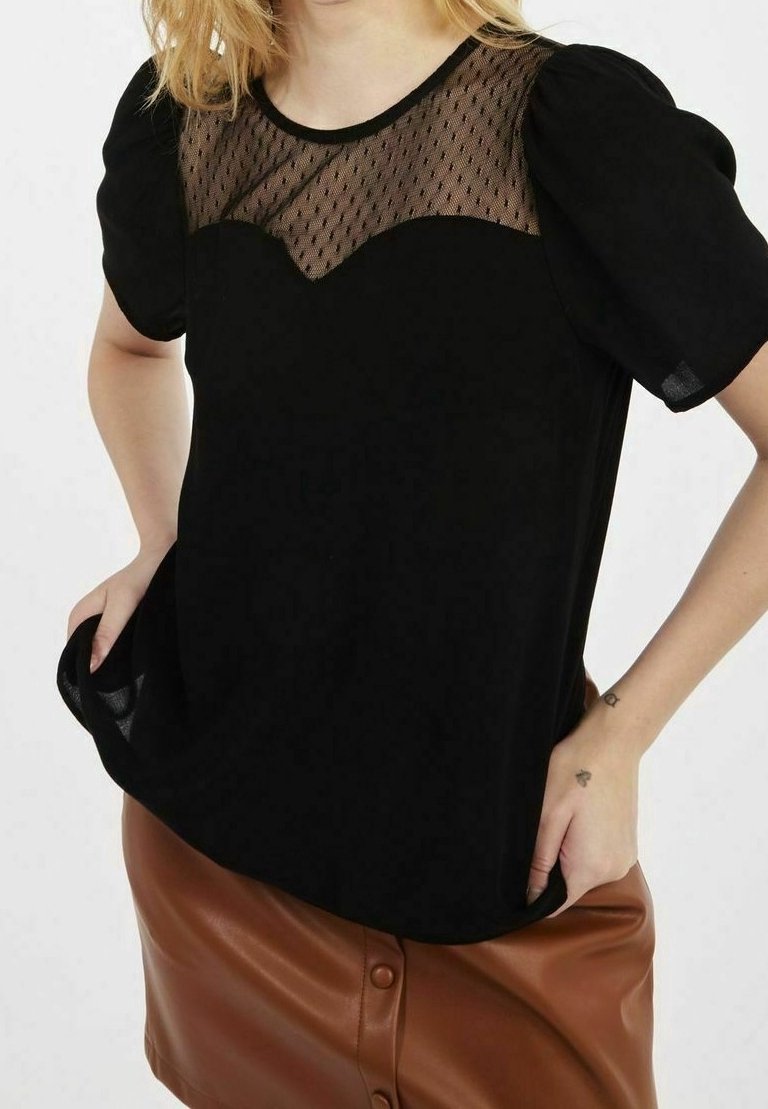 Svart topp med en nät-yoke med prickigt mönster, korta puffärmar och avslappnad passform. Matchas med en brun faux läderkjol.