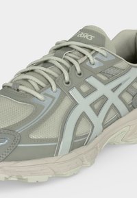 Ανοιχτό γκρι αθλητικό παπούτσι Asics για τρέξιμο με υφαντό διχτυωτό ύφασμα, επενδυμένο περιμετρικά, κορδόνια και χοντρή λαστιχένια σόλα με λεπτομερές πέλμα.