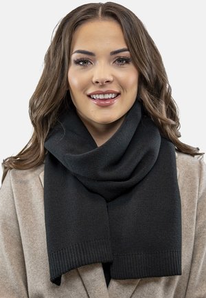 Écharpe noire en tricot avec une texture douce, présentant un design large et drapé et des extrémités côtelées, portée sur un manteau de couleur claire.