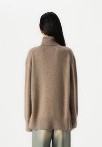Maglione a collo alto marrone, con vestibilità ampia, dotato di polsini e orlo a costine; realizzato in morbido materiale a maglia, presenta un alto collo e una texture liscia.