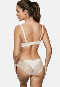 Soutien-gorge en dentelle beige avec des bretelles ajustables et fermeture à crochet, accompagné de culottes en dentelle assorties avec des motifs floraux sur les côtés.