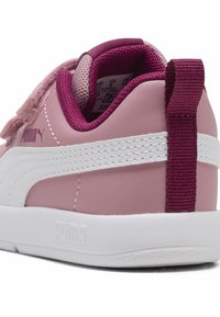 Rosa-weiße Sneaker mit einer glatten Lederoberfläche, Klettverschluss und einem strukturierten kastanienbraunen Akzent an der Ferse. Prägung des Logos an der Seite.