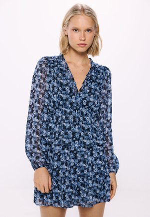Floral dress featuring a blue and black pattern, sheer fabric, v-neckline, puffed long sleeves, and a tiered ruffled hem.