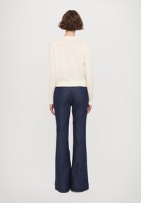 Ljusgrön långärmad tröja i cream som kombineras med mörkblå utsvängda denimjeans med orange sömmar och hög midja.