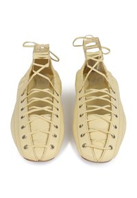 Chaussures en cuir jaune avec une forme arrondie, présentant un design complexe avec des lacets et des œillets en argent. Texture douce avec des accents brodés.