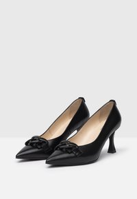 Black patent leather pointed-toe heels with a decorative bow detail at the front and a slender, angled heel. Smooth texture throughout.