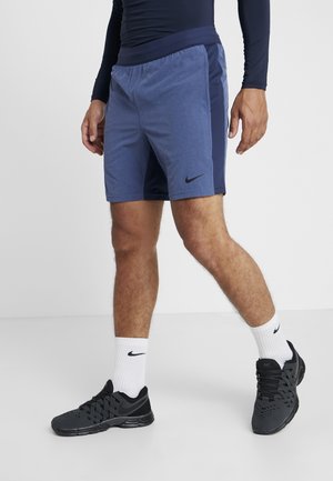 Nike shorts in blue with a dark blue side panel, elastic waistband, and a small black logo. Worn with black athletic shoes and white socks.
