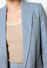 Blazer bleu clair à chevrons avec revers crantés, associé à un débardeur côtelé beige à encolure festonnée.