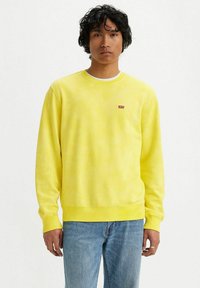 Geel crewneck sweatshirt van zachte stof, met een klein rood Levi's logo op de borst, gecombineerd met blauwe denim jeans.