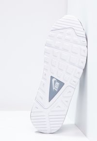 Witte rubberen sneakerzool met een gestructureerd grippatroon, voorzien van een grijs Nike-logo in een driehoekige uitsnede aan de zijkant.
