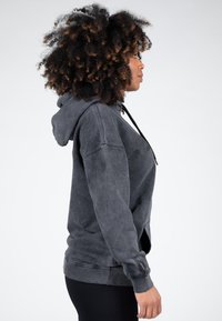 Grijze, oversized hoodie met een trekkoord, ribbelmanchetten en geribbelde onderrand. Het heeft een gewassen textuur en een buidelzak. Zijaanzicht.