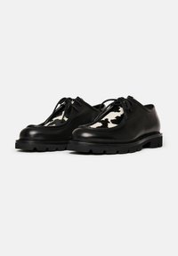 Scarpe in pelle nera con un pannello a motivo bianco e nero texturizzato. Presentano punta rotonda, design stringato e suola spessa in gomma.