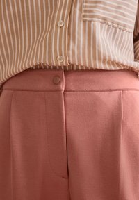 Chemise à rayures marron clair boutonnée, associée à un pantalon taille haute texturé de couleur rose, doté d'un bouton latéral et de plis.