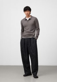 Polo grigio a maniche lunghe con colletto, abbinato a pantaloni neri larghi e strutturati. L'outfit presenta un design semplice e modelli minimali.