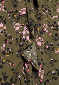 Tecido com padrão floral em verde-azeitona apresenta flores em rosa, amarelo e preto, com uma superfície suave e texturizada e um design em camadas.