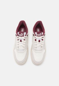 Zapatillas blancas con acentos burdeos, que cuentan con un collar acolchado, materiales de serraje y cuero, detalles perforados y un diseño con cordones.