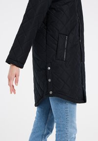 Giacca nera trapuntata con tasca laterale con zip e bottoni a pressione argentati. Presenta una vestibilità comoda e maniche lunghe, abbinata a jeans blu.