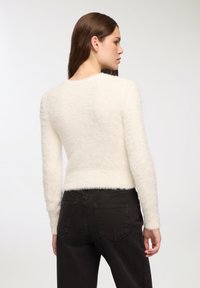 Maglione morbido di colore crema con maniche lunghe e scollatura rotonda, abbinato a jeans scuri e aderenti con tasche posteriori.