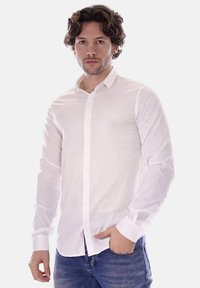 Camicia bianca con bottoni realizzata in tessuto leggero, dotata di maniche lunghe, colletto classico e un logo discreto sul petto.