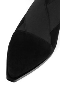 Musta mokkanahkainen kärkiosalta terävä kenkä, jossa leveät, ristikkäiset joustavat hihnat päällä.