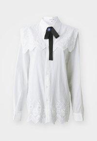 Hvit skjorte med krage og brodert blomsterdesign, blondebesetning, og en svart sløyfe med blå dekorasjon. Lange ermer.