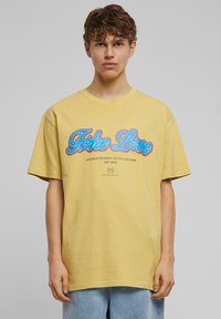 Gul bomulds t-shirt med korte ærmer, prydet med blå og røde kursiv-tekst "Take Love" og småtryk nedenunder, afslappet pasform.