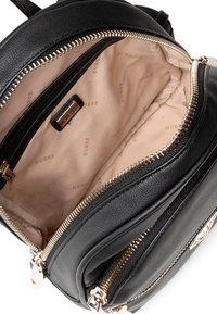 Sac à dos en faux cuir noir avec quincaillerie dorée, compartiments à double zip et intérieur beige doublé avec un logo de marque répété.