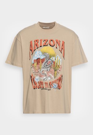 Beżowa, oversize koszulka z kolorową grafiką węża, kaktusów i napisem "ARIZONA ESCAPE TO NATURE". Wykonana z miękkiego materiału bawełnianego.